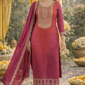 Puede incluir: Un salwar kameez magenta y naranja con bordados dorados. La túnica de manga larga presenta un escote y puños detallados, con una dupatta a juego. El atuendo tiene un estampado de lunares y se combina con pantalones magenta. El conjunto es adecuado para ocasiones festivas.