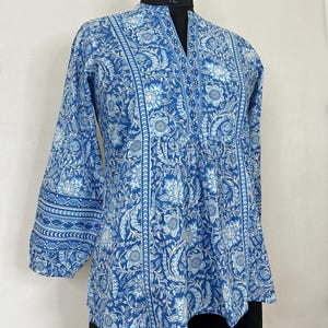 May include: A blue and white floral print top with a V-neck and three-quarter sleeves. The top has a gathered waist and a slightly flared hem.