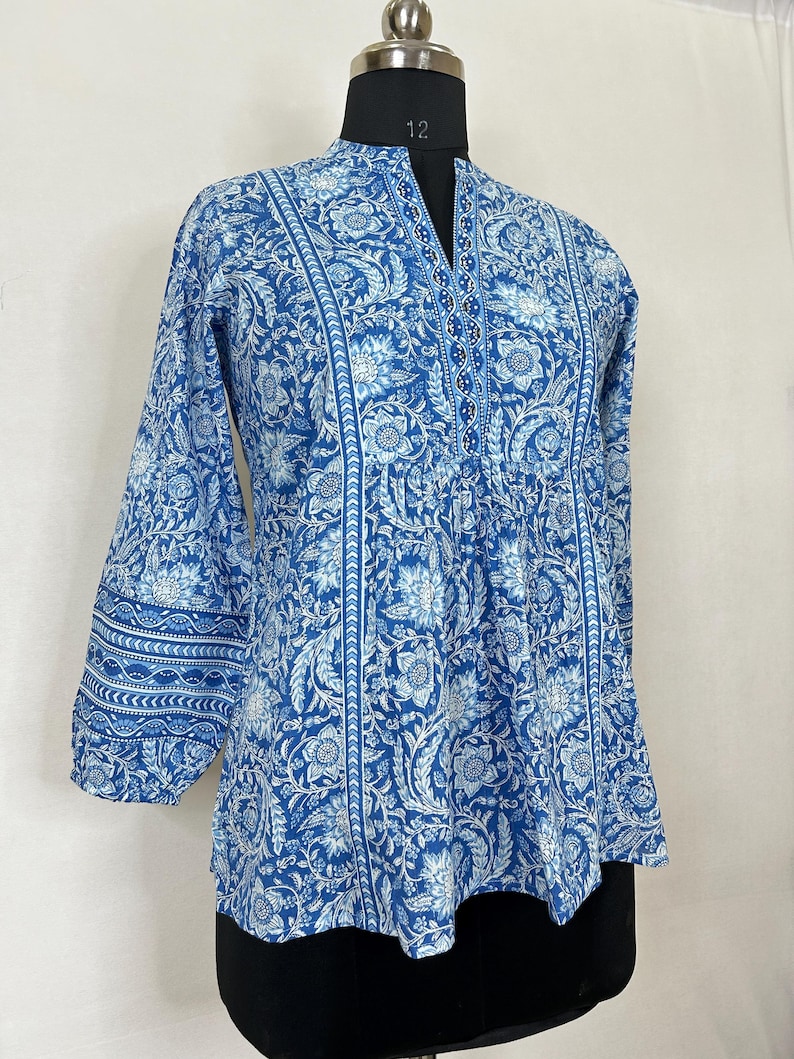 May include: A blue and white floral print top with a V-neck and three-quarter sleeves. The top has a gathered waist and a slightly flared hem.