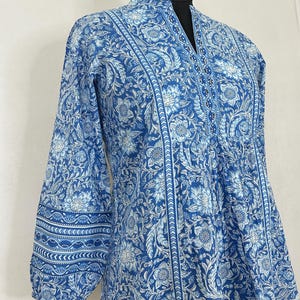 May include: A blue and white floral print cotton top with a mandarin collar and three-quarter sleeves. The top has a gathered waist and a decorative beaded neckline.