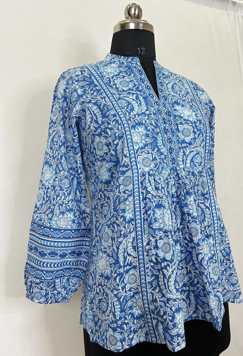 May include: A blue and white floral print cotton top with a mandarin collar and three-quarter sleeves. The top has a gathered waist and a decorative beaded neckline.
