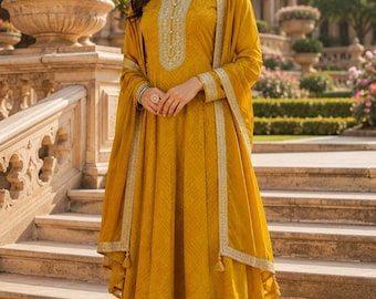 May include: A mustard yellow A-line kurta dress featuring a subtle geometric pattern, a round neckline with intricate silver embroidery, long sleeves, and a matching dupatta with silver trim. The dress is paired with matching mustard yellow trousers.