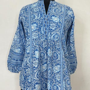 May include: A blue cotton top with a white floral print and a V-neck. The top has a gathered waist and 3/4 sleeves.