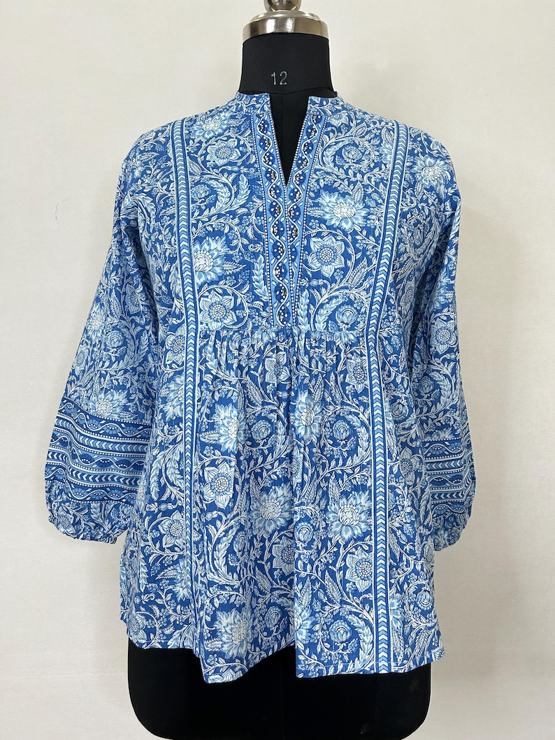 May include: A blue cotton top with a white floral print and a V-neck. The top has a gathered waist and 3/4 sleeves.