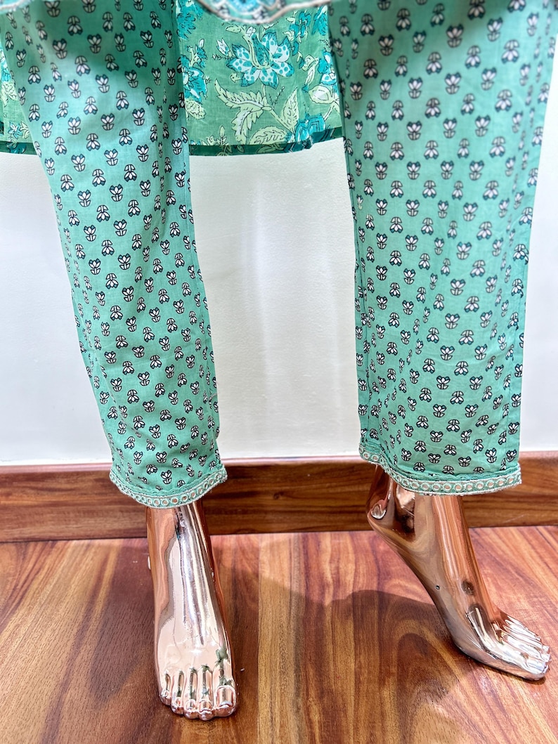 May include: Mint green pants with a repeating floral pattern in black and white. The pants have a decorative trim at the hem. The top of the pants is visible, featuring a floral design in shades of green and blue.