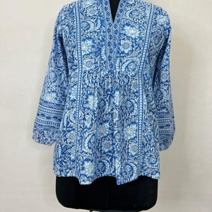 May include: A blue and white floral print cotton top with a V-neck and 3/4 sleeves. The top has a gathered waist and a relaxed fit.