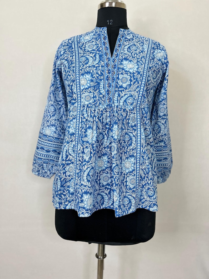 May include: A blue and white floral print cotton top with a V-neck and 3/4 sleeves. The top has a gathered waist and a relaxed fit.