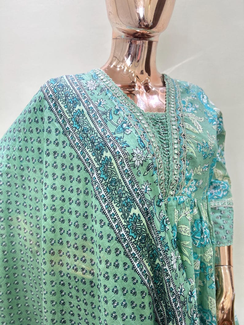 May include: A light green floral print dress with a matching scarf. The dress features a square neckline and long sleeves. The scarf and dress have a repeating pattern of white and teal floral designs.