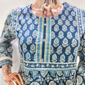 May include: A blue long-sleeve dress with a white paisley pattern. The dress features a round neckline, decorative buttons, and a contrasting stripe down the center. The sleeves have a lace trim.