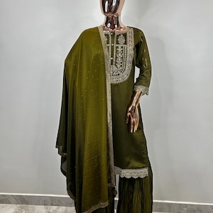 May include: A green embroidered kurta with a matching dupatta and palazzo pants. The kurta has a gold embroidered neckline and a lace trim. The dupatta is sheer and has a gold embroidered border. The palazzo pants are pleated and have a lace trim.