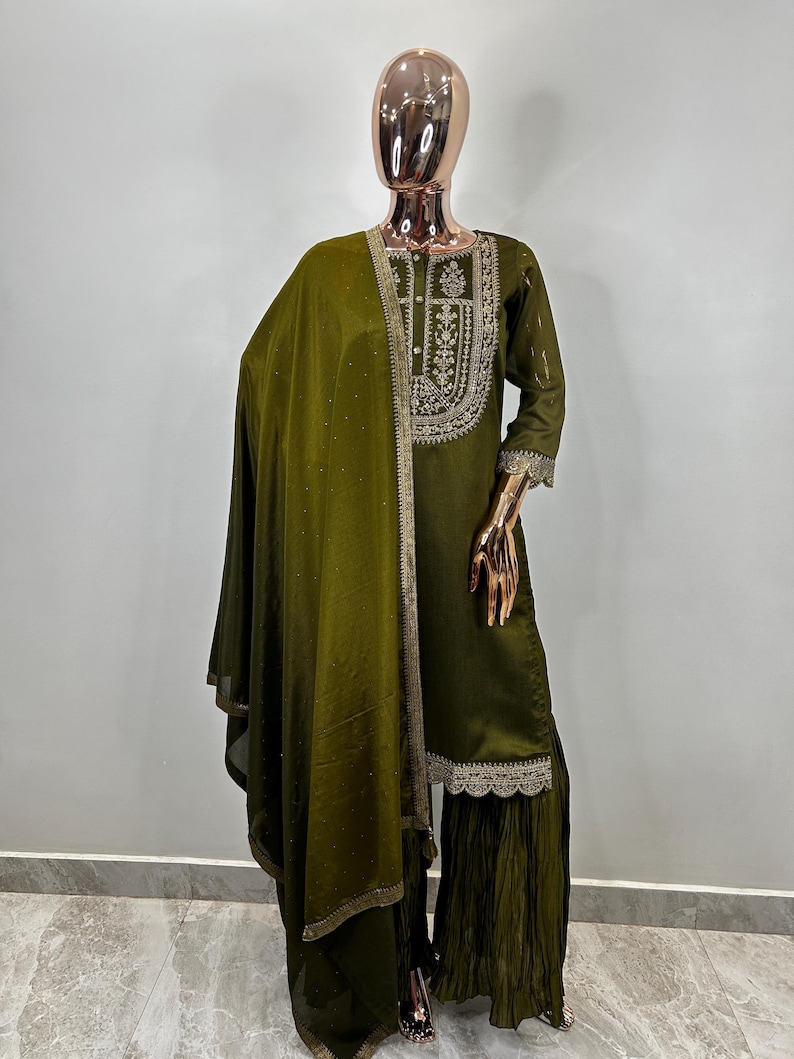 May include: A green embroidered kurta with a matching dupatta and palazzo pants. The kurta has a gold embroidered neckline and a lace trim. The dupatta is sheer and has a gold embroidered border. The palazzo pants are pleated and have a lace trim.