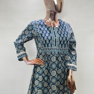 May include: A blue tunic with a white and blue pattern. The tunic has three-quarter sleeves with lace trim and a round neckline. The garment is displayed on a mannequin.
