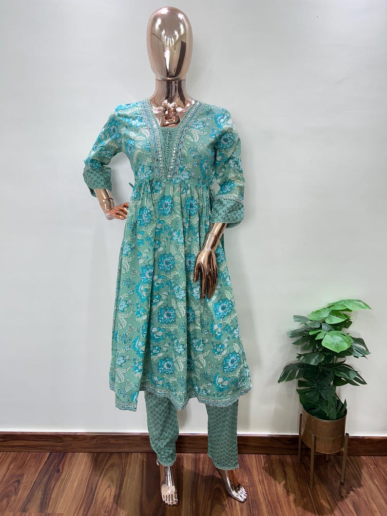 May include: A mint green floral print kurta set on a mannequin. The set includes a long-sleeved tunic with a V-neck and matching pants. The floral pattern features blue and white flowers. The mannequin has a gold-colored head and hands.