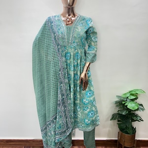 May include: A mint green floral print salwar kameez set displayed on a mannequin. The set includes a long-sleeved tunic, matching pants, and a patterned scarf. The tunic and pants feature a floral design in shades of blue and green.