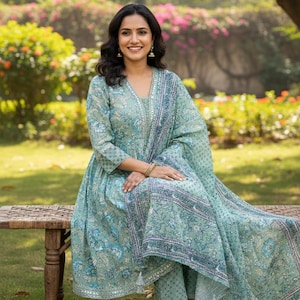 May include: A light teal Indian salwar kameez set with a floral pattern and a matching dupatta. The outfit features a V-neckline and is worn with matching pants. The ensemble is adorned with a detailed border.
