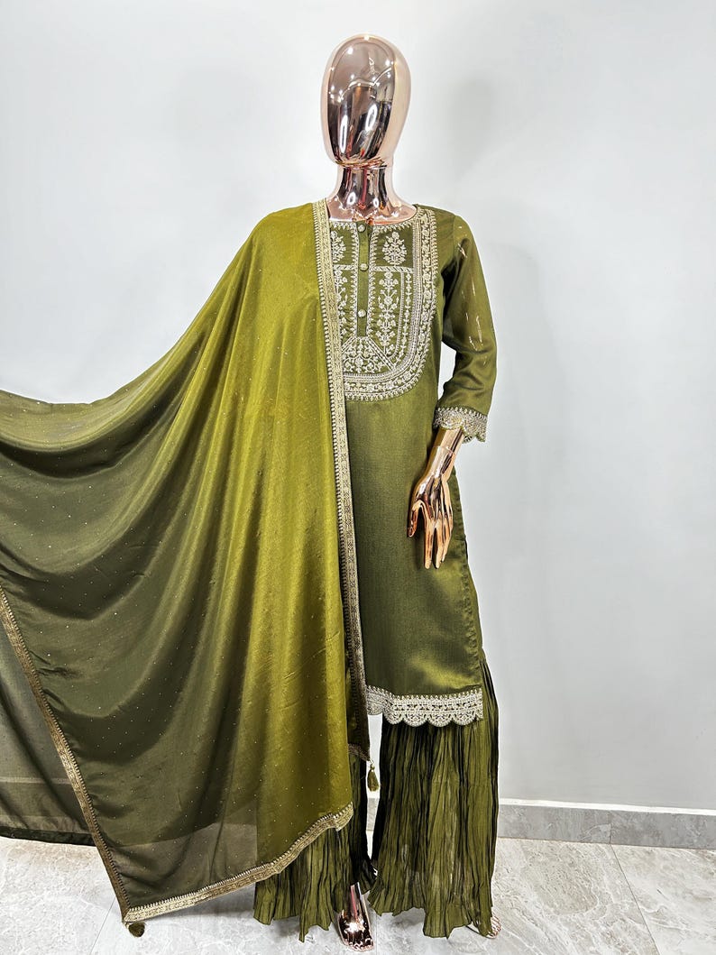 May include: A green embroidered kurta with a matching dupatta and palazzo pants. The kurta has a round neckline and three-quarter sleeves. The dupatta is sheer and has a gold border. The palazzo pants are pleated and have a lace trim.