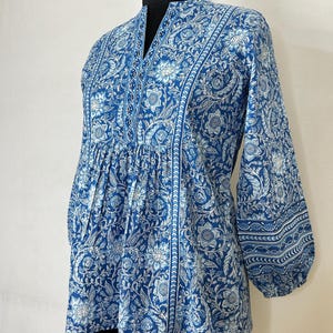 May include: A blue and white floral printed top with a mandarin collar and 3/4 sleeves. The top has a gathered waist and a slightly flared hem.
