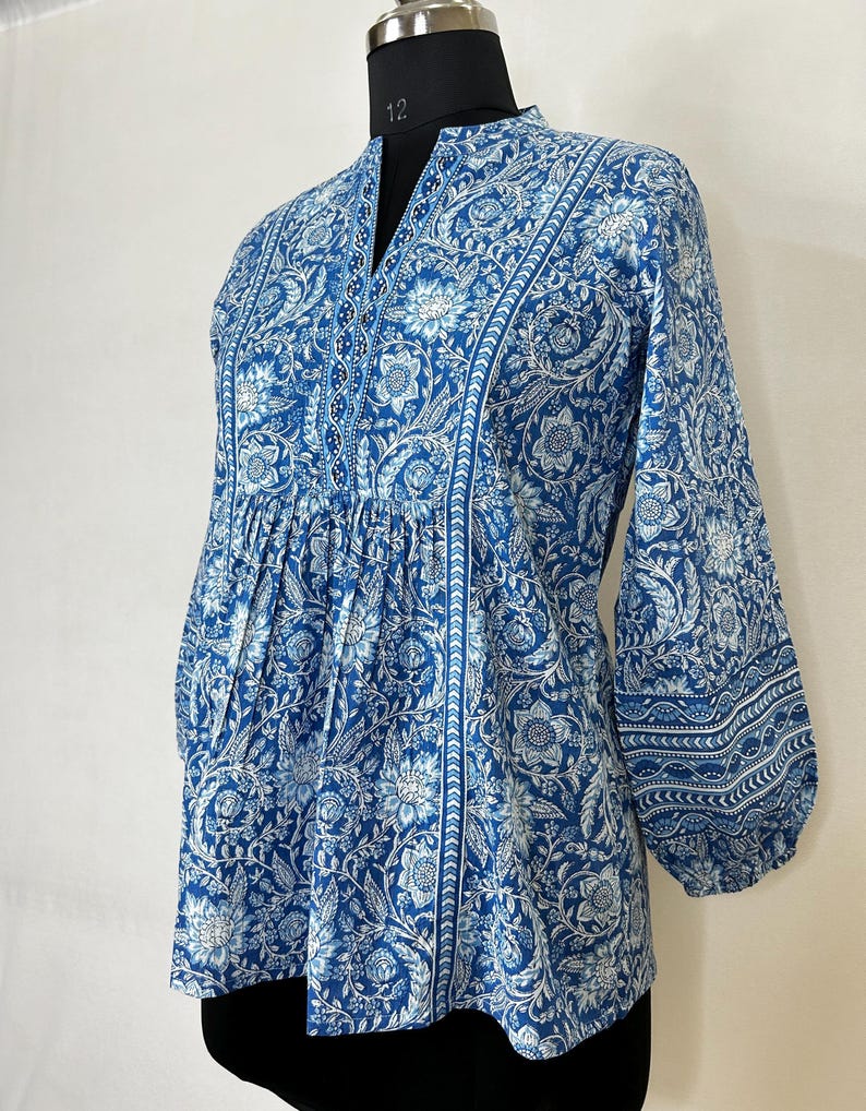 May include: A blue and white floral printed top with a mandarin collar and 3/4 sleeves. The top has a gathered waist and a slightly flared hem.
