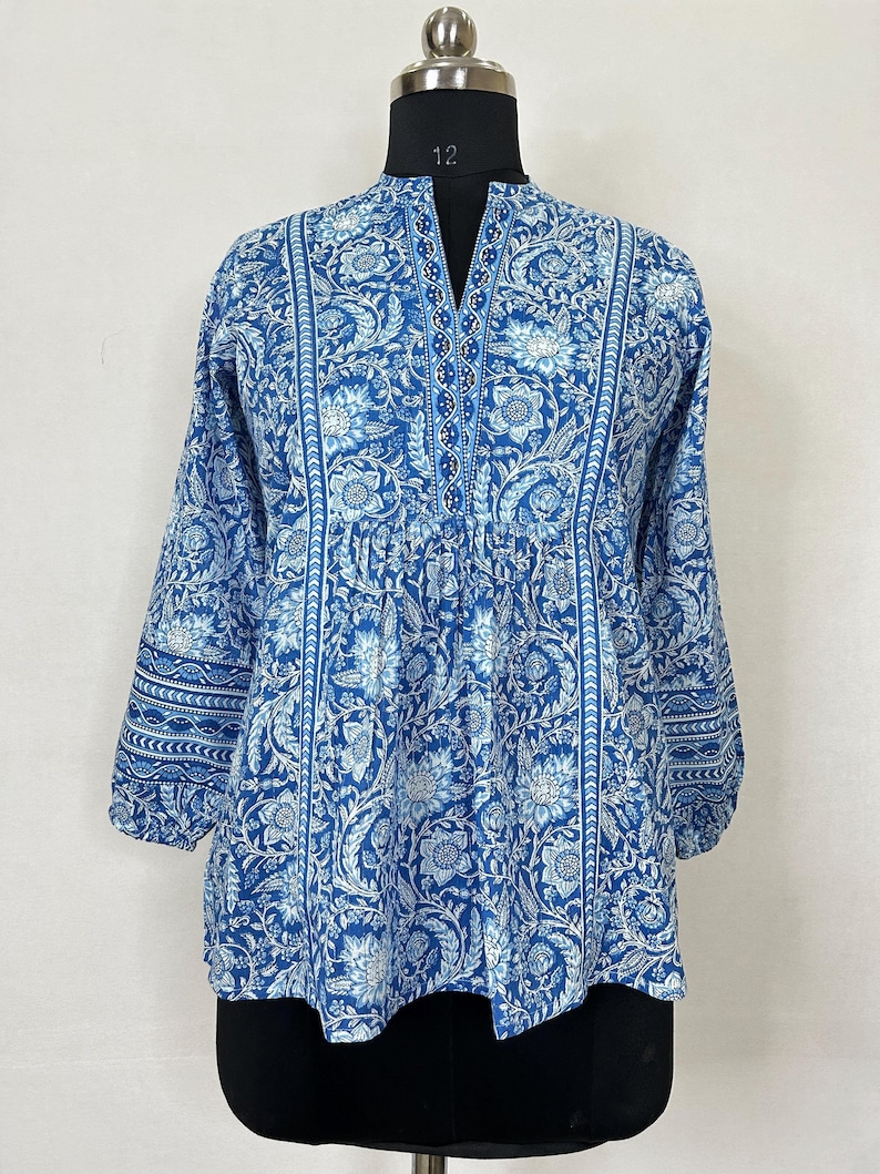 May include: A blue and white floral print cotton tunic top with a V-neck and 3/4 sleeves. The top has a beaded trim along the neckline and a gathered waist.