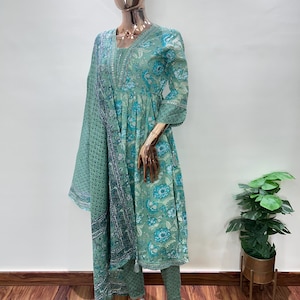 May include: A mint green Indian salwar kameez set displayed on a mannequin. The outfit features a floral print in shades of blue and white. The set includes a tunic, pants, and a matching scarf. The tunic has a V-neck and three-quarter sleeves.