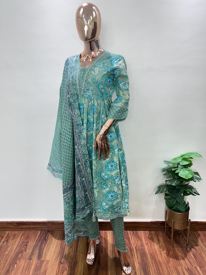 May include: A mint green Indian salwar kameez set displayed on a mannequin. The outfit features a floral print in shades of blue and white. The set includes a tunic, pants, and a matching scarf. The tunic has a V-neck and three-quarter sleeves.