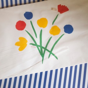 May include: A white paper with a colourful flower design painted in red, yellow, blue and green. The flowers are stylised and abstract. The paper has a signature in the bottom left corner.