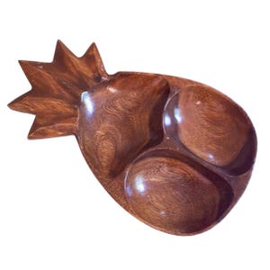 Könnte beinhalten: Eine Holzservierschale in Form einer Ananas. Die Schale ist in drei Abschnitte unterteilt und hat eine dunkelbraune Oberfläche. Die Ananas-Oberseite ist sternförmig.