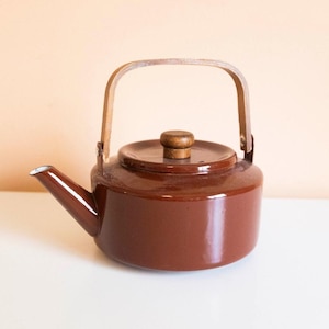 以下が含まれることがあります： 光沢のある茶色のティーポットで、円筒形の本体、短い角度のついた注ぎ口、小さな木製のつまみが付いた平らな蓋が特徴です。ティーポットには、側面に取り付けられた高くアーチ状の木製ハンドルがあり、滑らかな仕上げと対照的です。