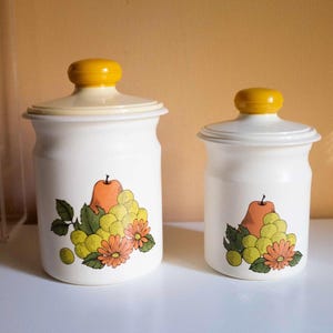 May include: A white ceramic mug with a black handle and the text "But First, Coffee" in a bold, black font. The mug is set against a blurred background, suggesting a cozy setting.