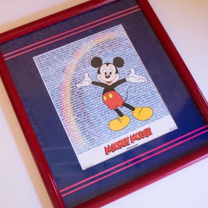 May include: A framed print of Mickey Mouse in a red, white, and blue frame. The print features Mickey Mouse in a red and yellow outfit with a rainbow behind him. The print says "Mickey Mouse" at the bottom.