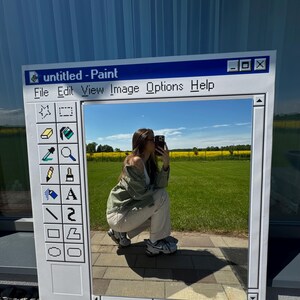 May include: A large, rectangular mirror designed to resemble the classic Windows Paint application interface. The mirror's frame is white with a blue top bar displaying the text "untitled - Paint". The mirror reflects a person and a sunny outdoor scene.