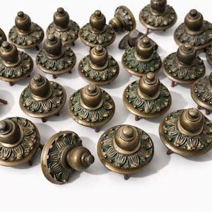 Puede incluir: Colección de tiradores de armario antiguos de latón. Cada tirador presenta un diseño floral detallado en la base y una parte superior redondeada. Los tiradores tienen una estética vintage, con una mezcla de bronce y pátina verde.