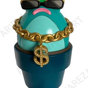 May include: A whimsical teal-colored figurine in a flower pot, sporting black sunglasses with gold trim, a gold chain, and a dollar sign pendant. The figurine has a green leaf and a pink mouth. The pot is dark teal.