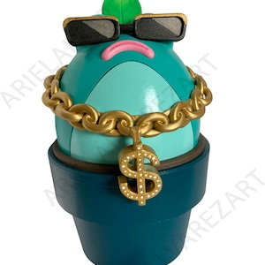 May include: A whimsical, turquoise-colored cactus figurine wearing black sunglasses and a gold chain with a dollar sign pendant. The cactus is in a dark teal pot, with a green leaf on top.
