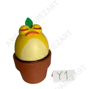 May include: A whimsical, hand-painted ceramic frog figurine in a brown pot. The frog is yellow with a white belly, closed red eyes, and a green leaf on its head. The pot is brown, and a small white tag with "Y1" is visible.