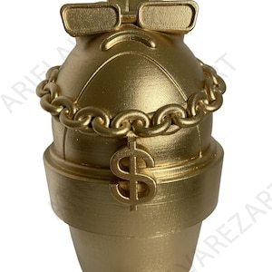May include: A gold-colored piggy bank with a unique design. It features a chain around the middle, a dollar sign pendant, and sunglasses. The piggy bank is shaped like a flower pot and has a decorative top.