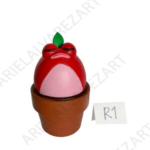 May include: A whimsical, hand-painted red frog figurine with a pink belly and closed eyes, topped with a green leaf. The frog sits in a brown flower pot, creating a unique decorative piece.