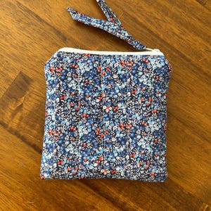 Könnte beinhalten: Ein kleiner, gesteppter Beutel mit einem Blumenmuster in Blau-, Rot- und Weißtönen. Der Beutel hat einen weißen Reißverschluss und einen passenden Stoffzug. Der Beutel ist rechteckig und scheint handgefertigt zu sein.