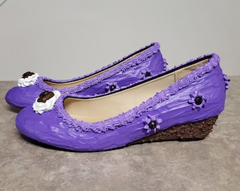 May include: A pair of purple wedge heel flats with decorative frosting-like trim and embellishments. The shoes have a brown textured wedge heel and are decorated with white and brown accents.