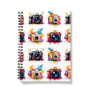 May include: A spiral bound notebook with a colourful design featuring cameras with paint splatters. The cameras are in various colours, including red, blue, green, yellow, and purple.