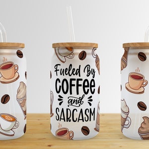 May include: Three white reusable coffee tumblers with lids and straws. The tumblers have a pattern of coffee cups, coffee beans and whipped cream. The middle tumbler has the text "Fueled By Coffee and Sarcasm".