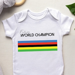 K&ouml;nnte beinhalten: Ein wei&szlig;er kurz&auml;rmeliger Babybody mit dem schwarzen Schriftzug Future WORLD CHAMPION &uuml;ber einem horizontalen Streifenmuster in den Farben Blau, Rot, Schwarz, Gelb und Gr&uuml;n, das mittig auf der Brust aufgedruckt ist.