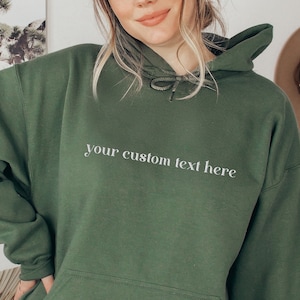 May include: A dark green hooded sweatshirt with the text "your custom text here" printed on the front.