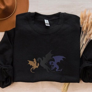 May include: Black sweatshirt featuring a graphic of three dragons in different colours: gold, black and purple.