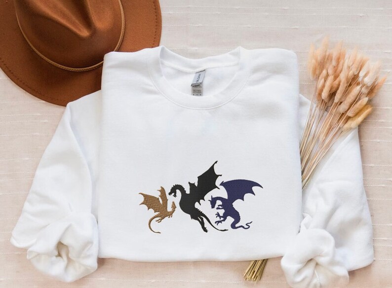 May include: White sweatshirt featuring a black, blue and gold silhouette of three dragons.