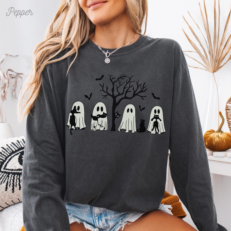 Puede incluir: Una sudadera gris oscuro de manga larga con un gr&aacute;fico de cinco fantasmas y gatos negros. Los fantasmas llevan sombreros y sostienen gatos. El gr&aacute;fico est&aacute; centrado en la sudadera y est&aacute; rodeado de un &aacute;rbol negro con ramas desnudas. El texto "Pepper" est&aacute; en la esquina superior izquierda de la imagen.