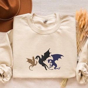 May include: A beige long-sleeved sweatshirt with a graphic of three black and blue dragons on the front.