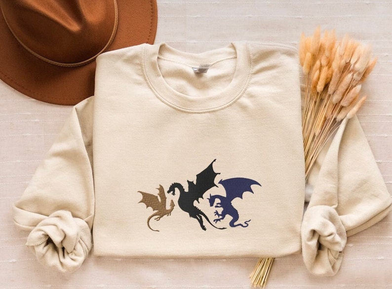 May include: A beige long-sleeved sweatshirt with a graphic of three black and blue dragons on the front.