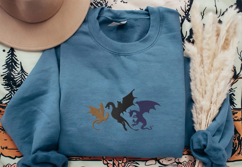 May include: A blue sweatshirt featuring a graphic of three black dragons with purple and brown accents.