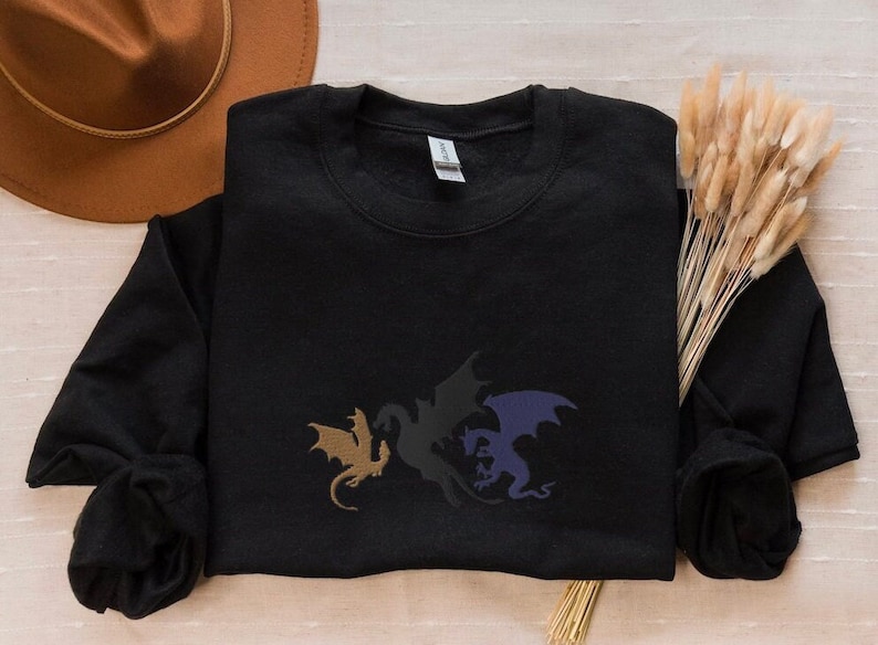 May include: Black sweatshirt featuring a graphic of three dragons in different colours: gold, black and purple.